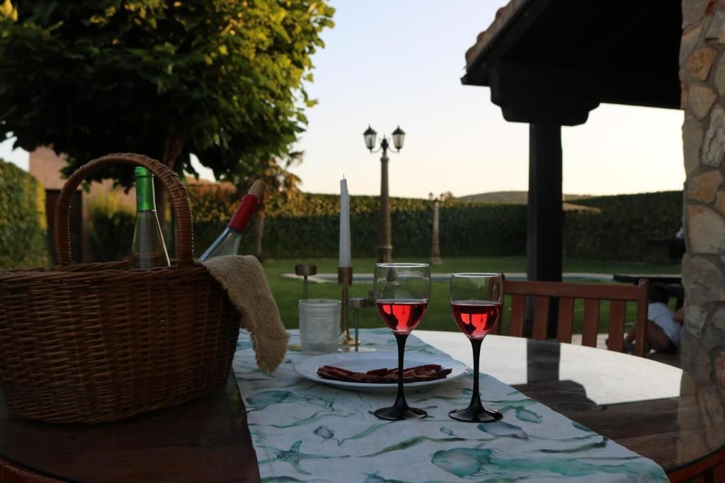 Mesa de exterior preparada para comer, con copas de vino, cesta y vela, sobre un fondo borroso.