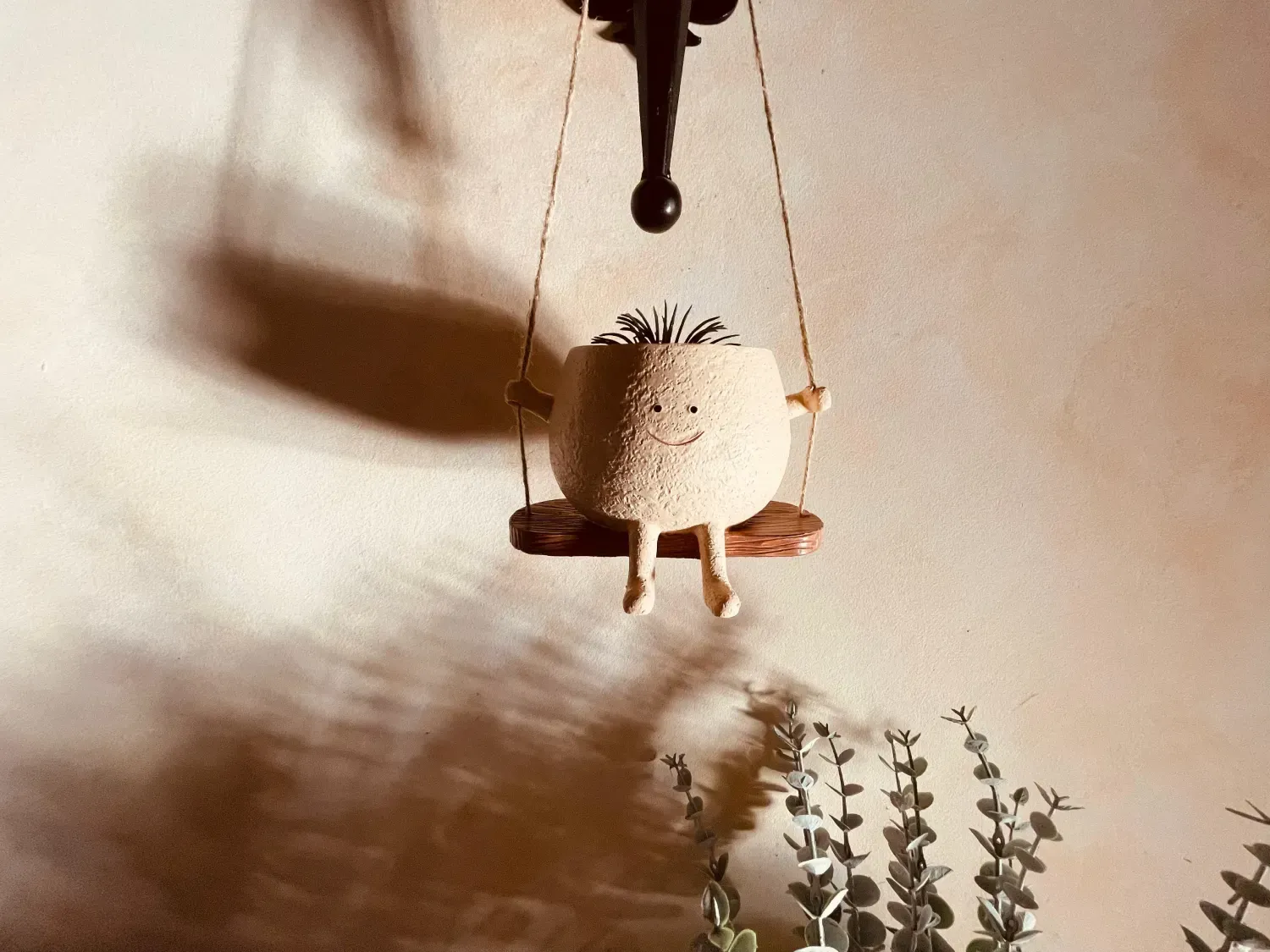 Maceta con detalle de cara, balanceándose en un columpio de madera.