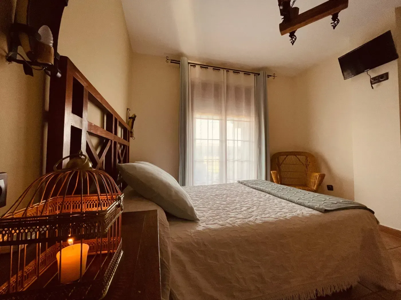 Dormitorio con gran cabecero de madera, cama, pequeña ventana, jaula de pájaros y silla.