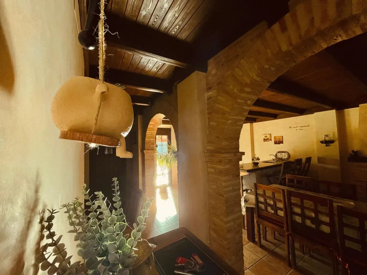Pasillo interior con arcos de piedra, techo de madera y jarra decorativa colgante.