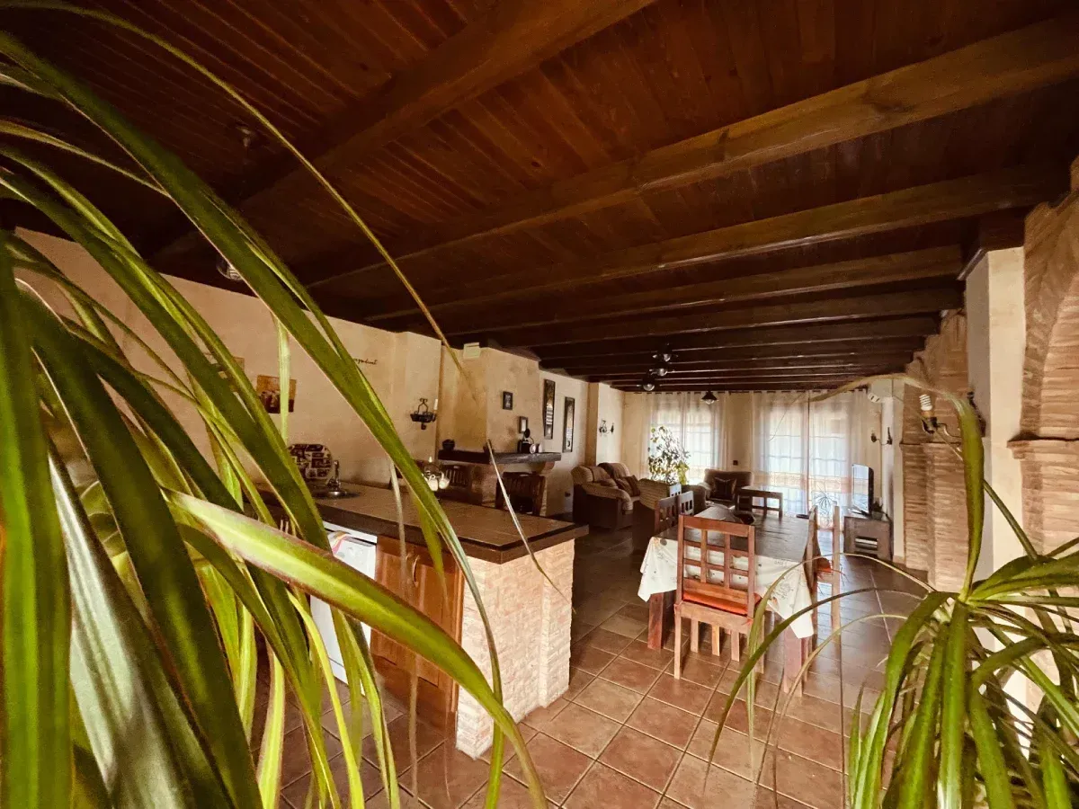 Vista interior de un espacio habitable con techo y vigas de madera, arcos de ladrillo y suelo de baldosas.