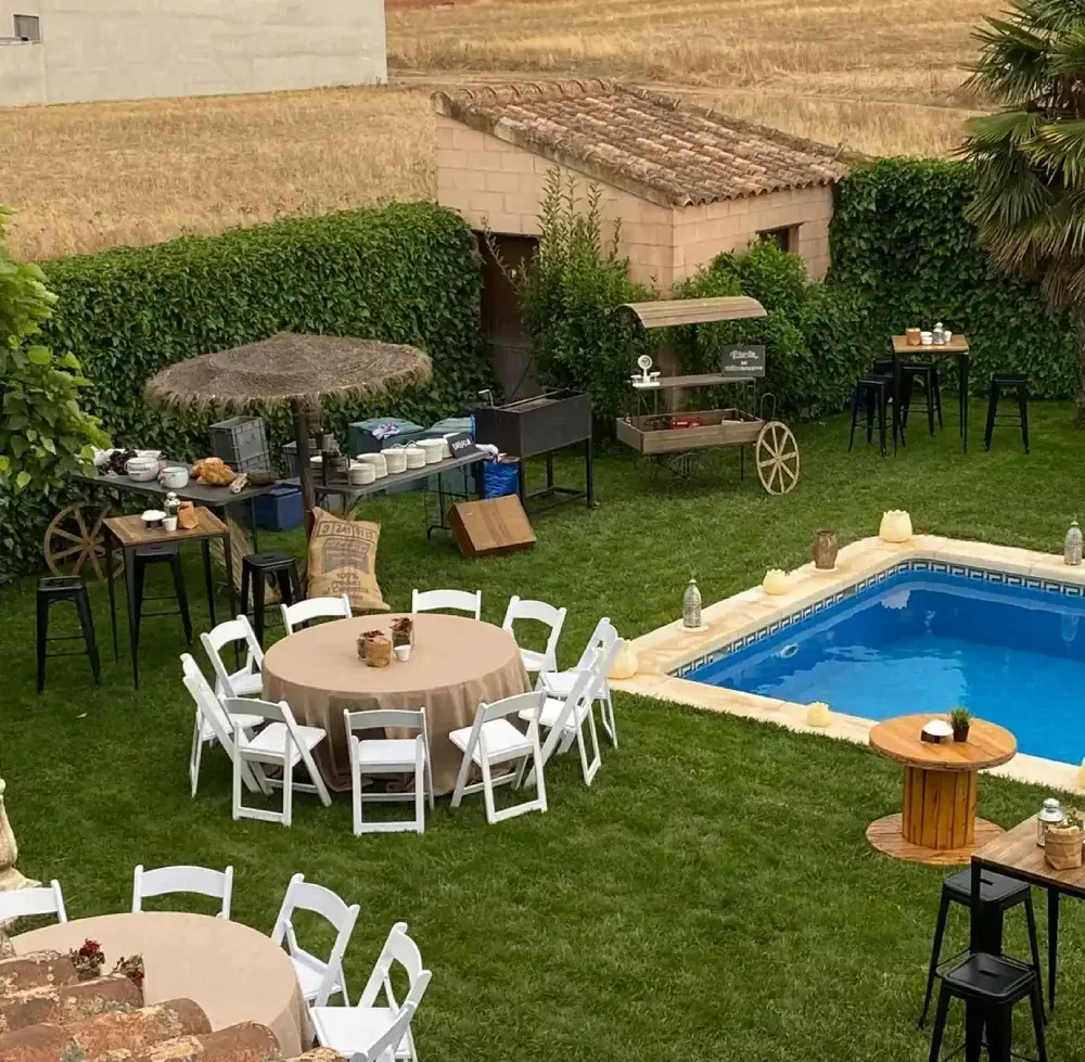 Fiesta en el patio con piscina, mesas redondas, buffet y carrito de bar.