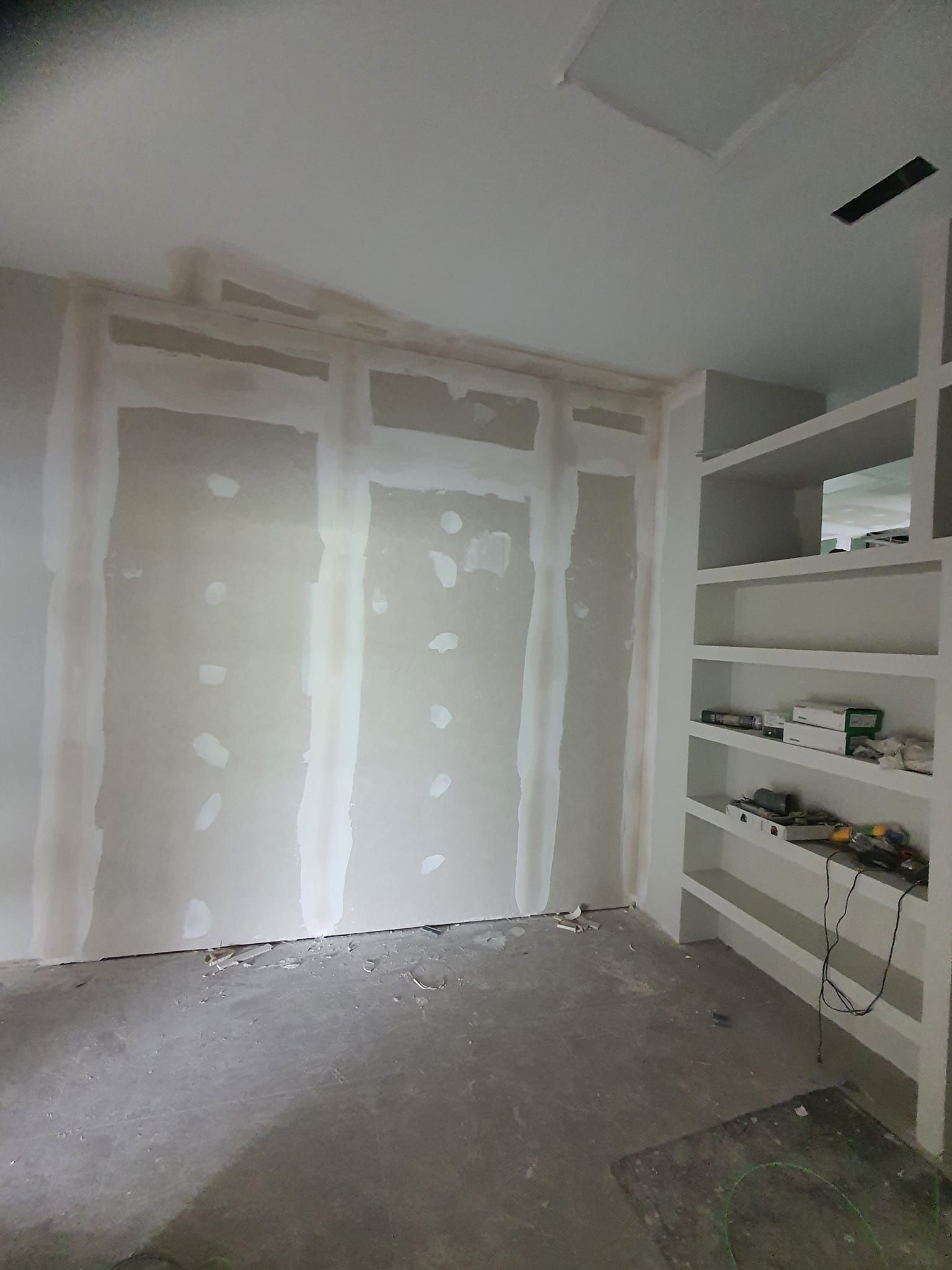 Paneles de yeso y estanterías empotradas en construcción en una habitación con escombros en el piso.
