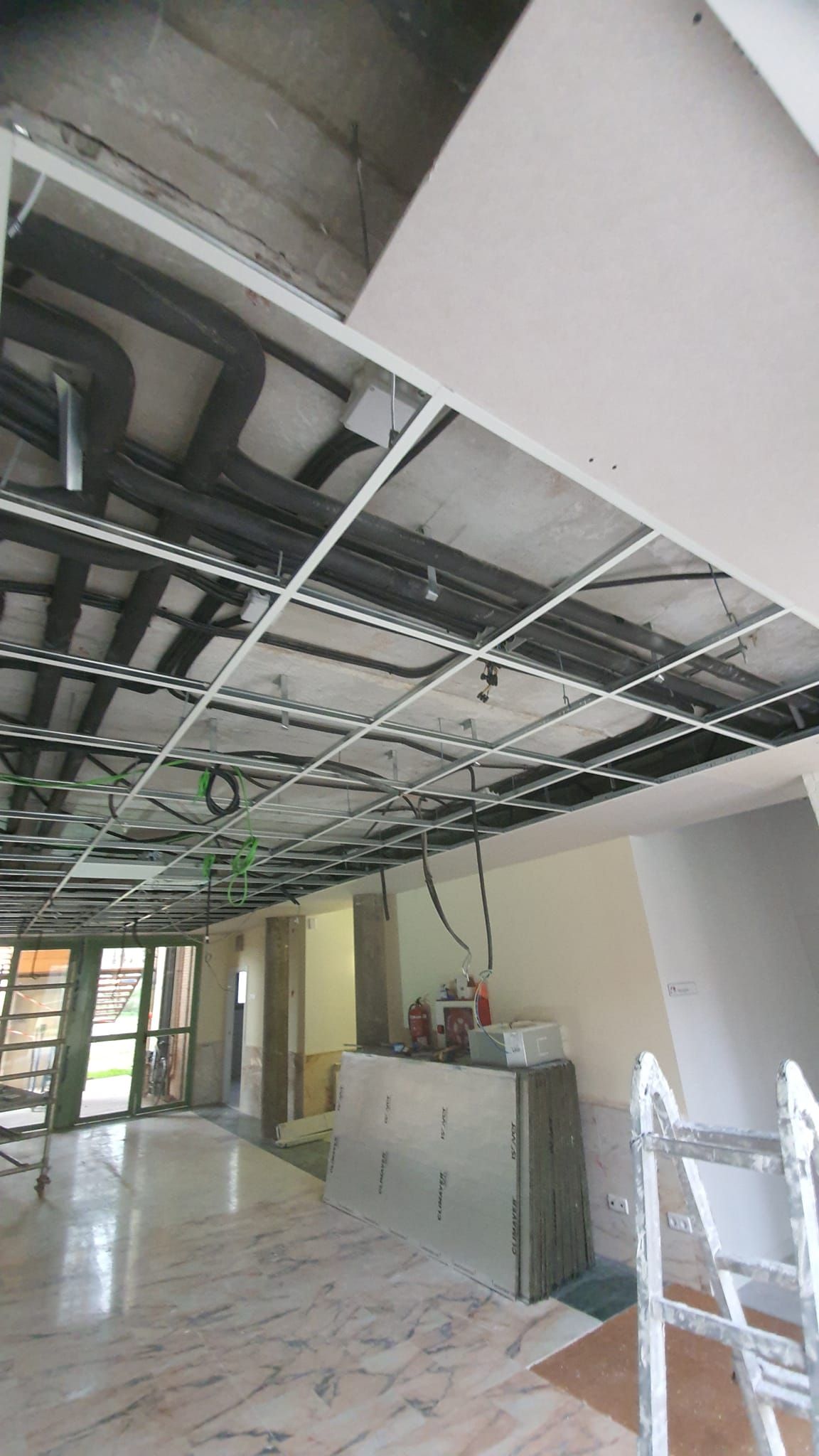 Interior de obra en construcción con rejilla de techo y conductos expuestos; habitación con piso de mármol y paredes parcialmente construidas.