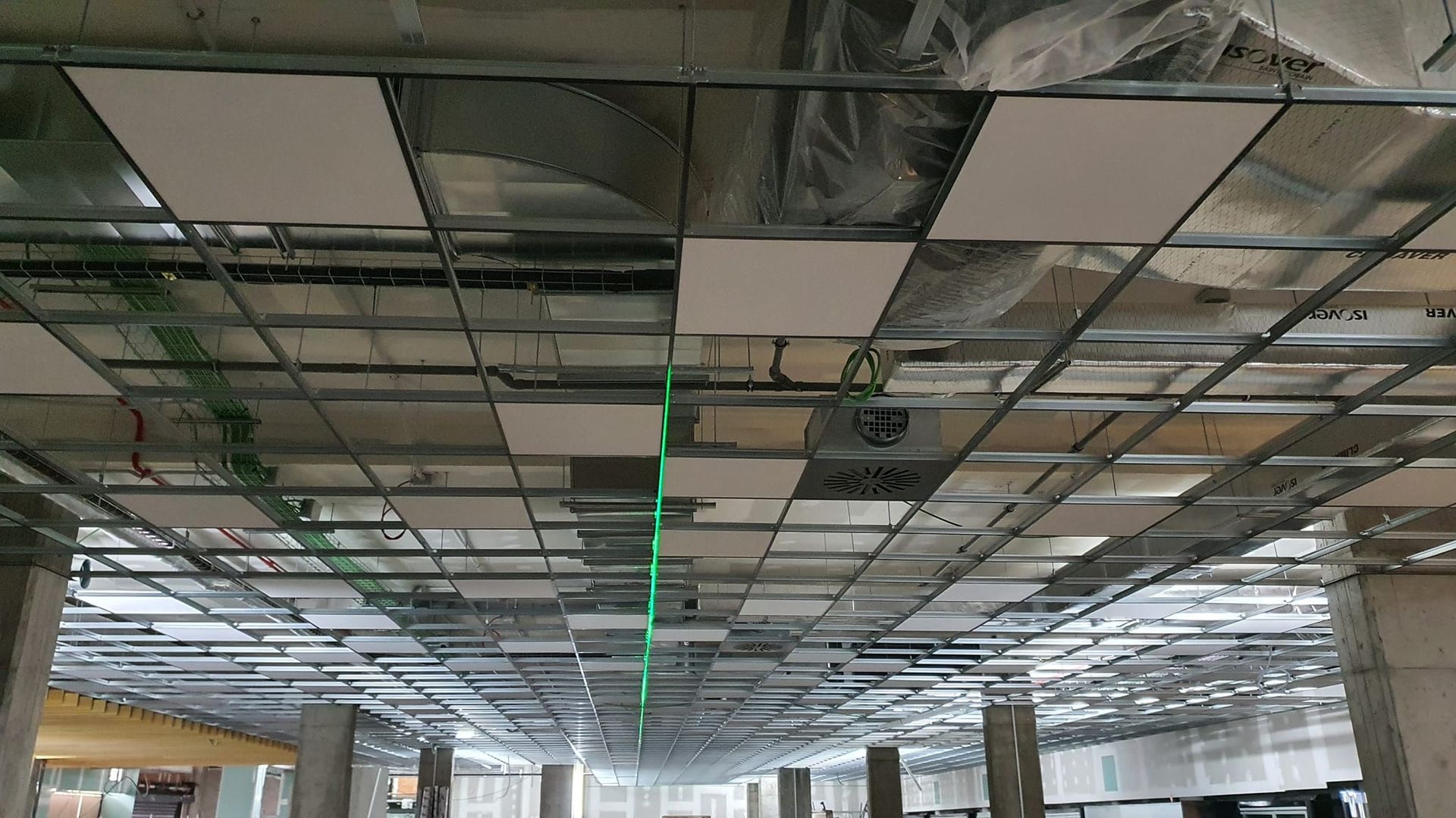 Techo en construcción con rejilla metálica, aislamiento y azulejos blancos. Línea de nivel láser verde.