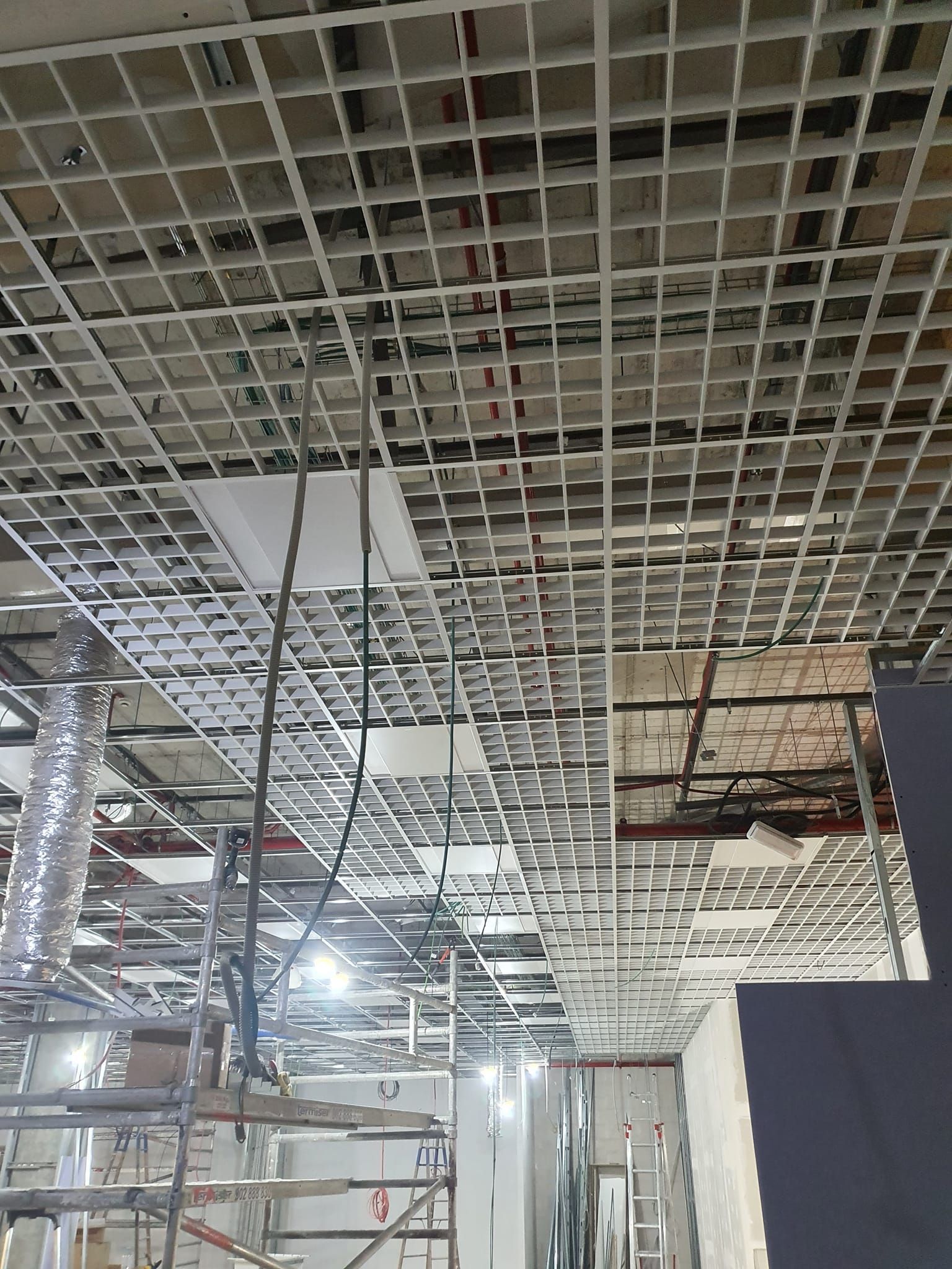 La construcción del techo de rejilla está en progreso; se ven andamios, cables y la infraestructura del edificio expuesta.