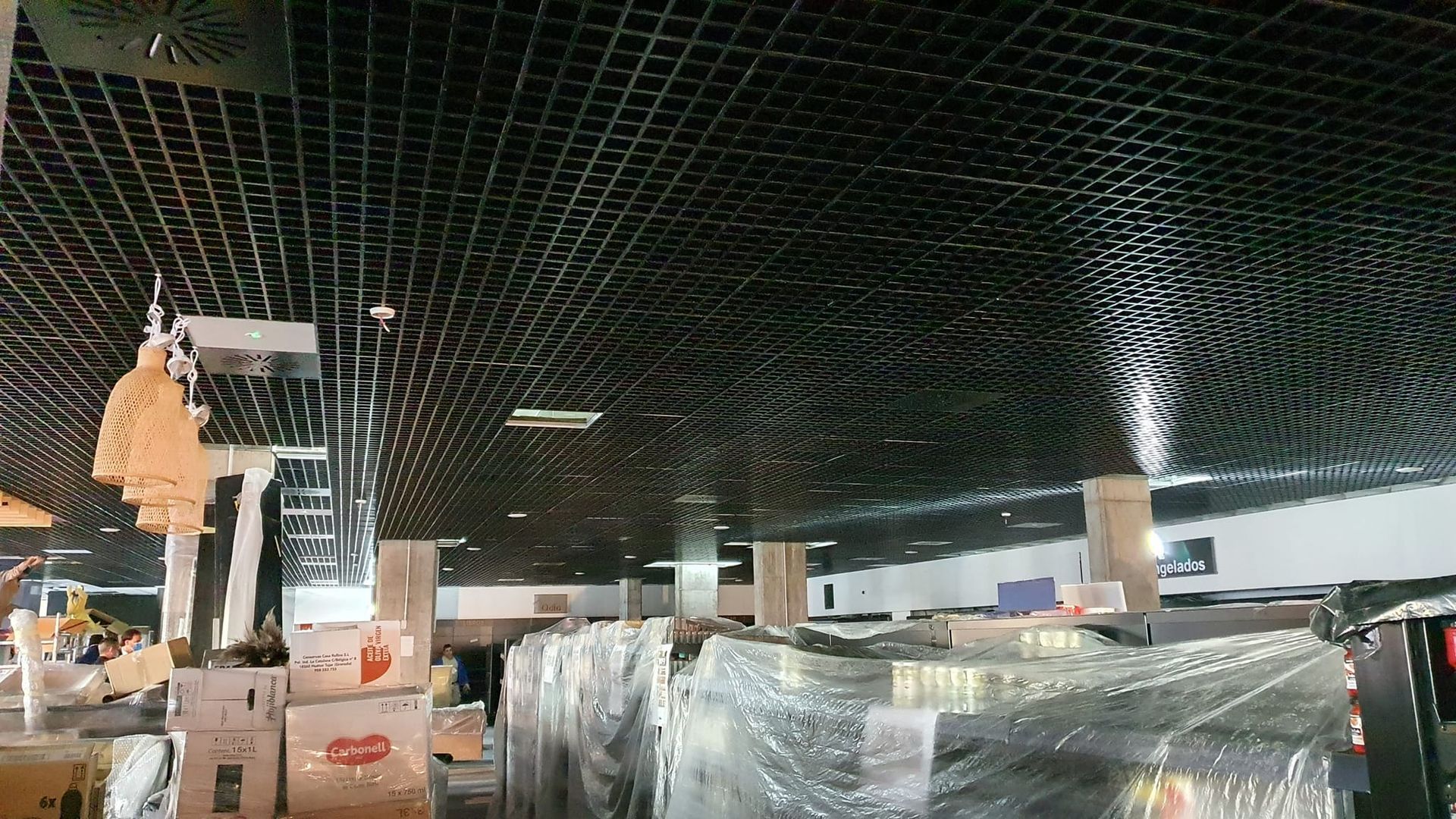 Techo de rejilla negra en un gran espacio interior, con ventilación visible y algo de mercancía debajo.