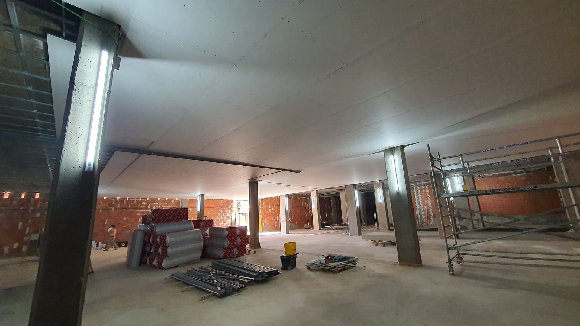 Interior de una obra en construcción con paredes de ladrillo visto, pilares de hormigón y andamios.