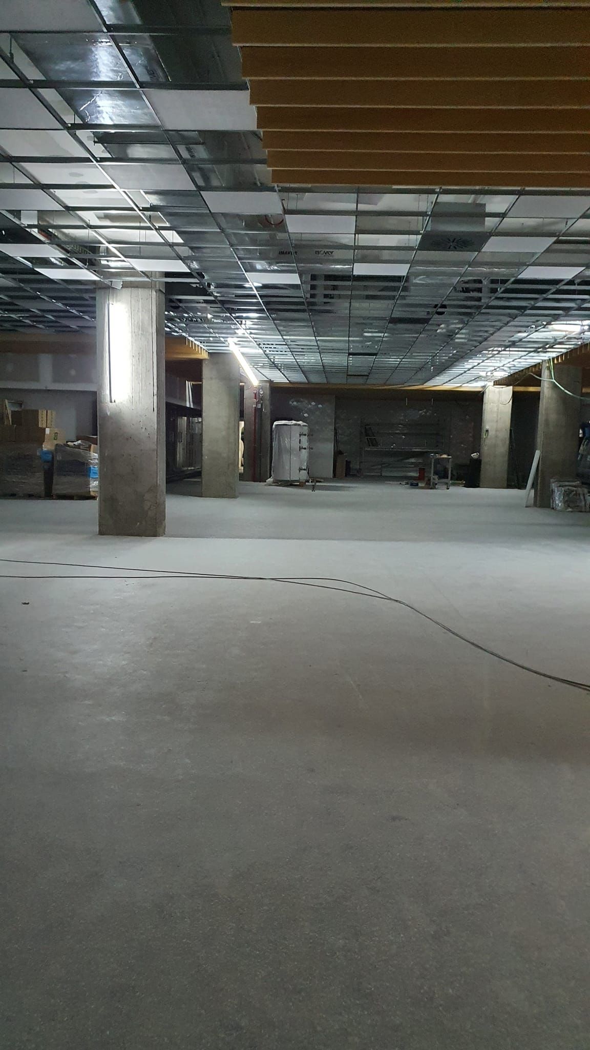 Local comercial vacío en construcción. Suelo de hormigón gris, techo con vigas vistas, pilares de soporte y paredes sin terminar.