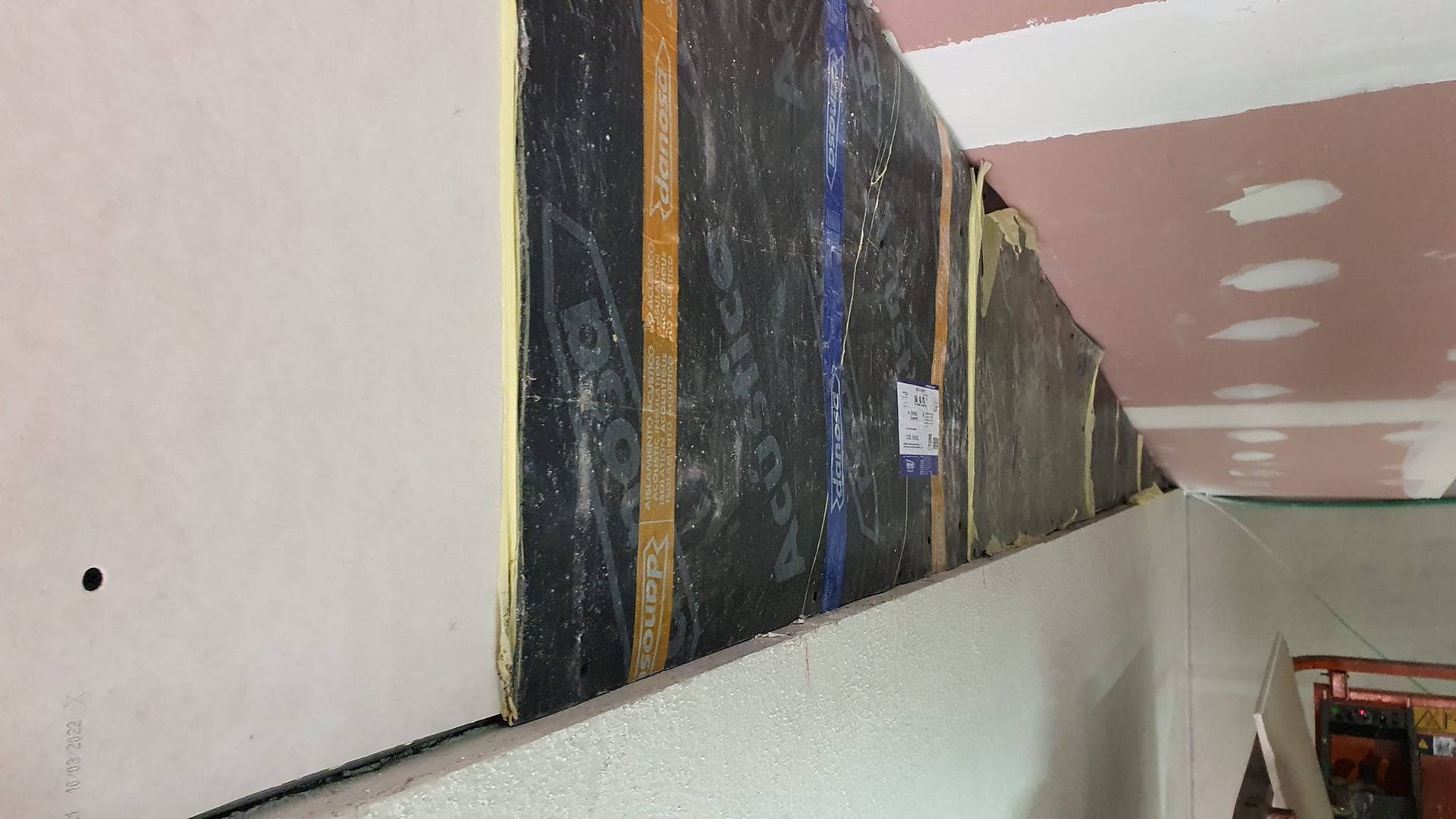 Interior del sitio de construcción: aislamiento negro expuesto y paneles de yeso, parcialmente cubiertos por placas de yeso.