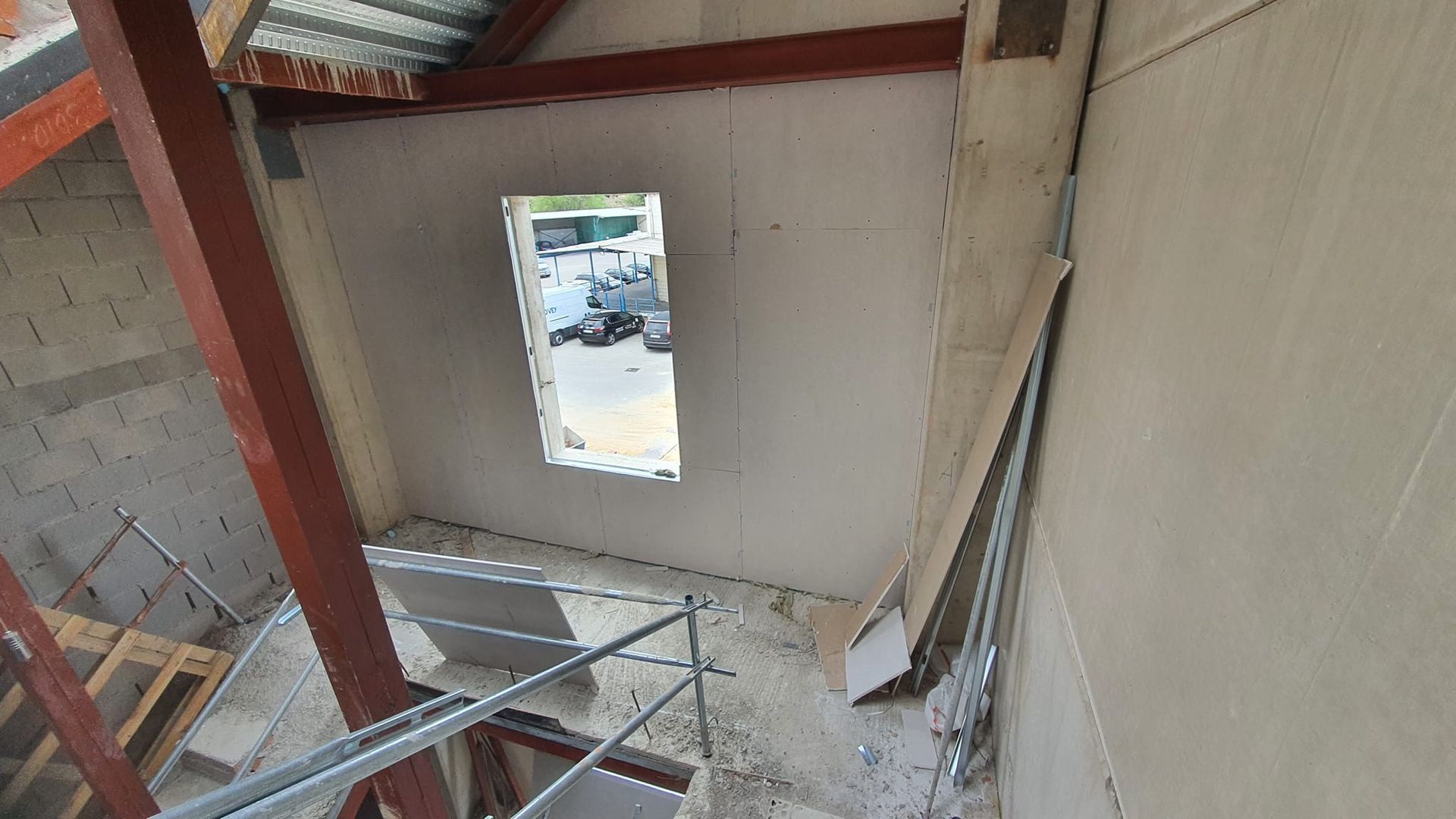 Vista interior de una habitación en construcción, con tragaluz, estructura metálica y vigas a la vista.