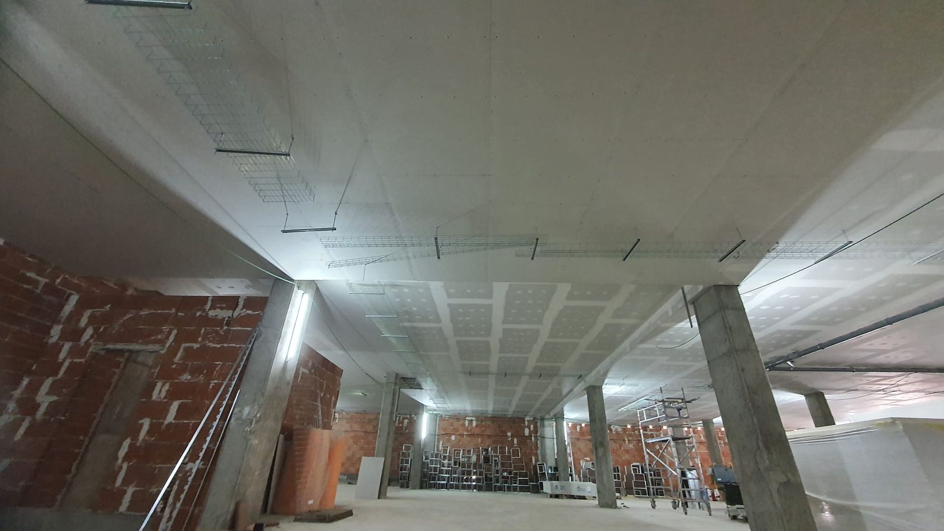 Interior en construcción con pilares de hormigón y paredes de ladrillo. Techo blanco y suelo sin terminar.