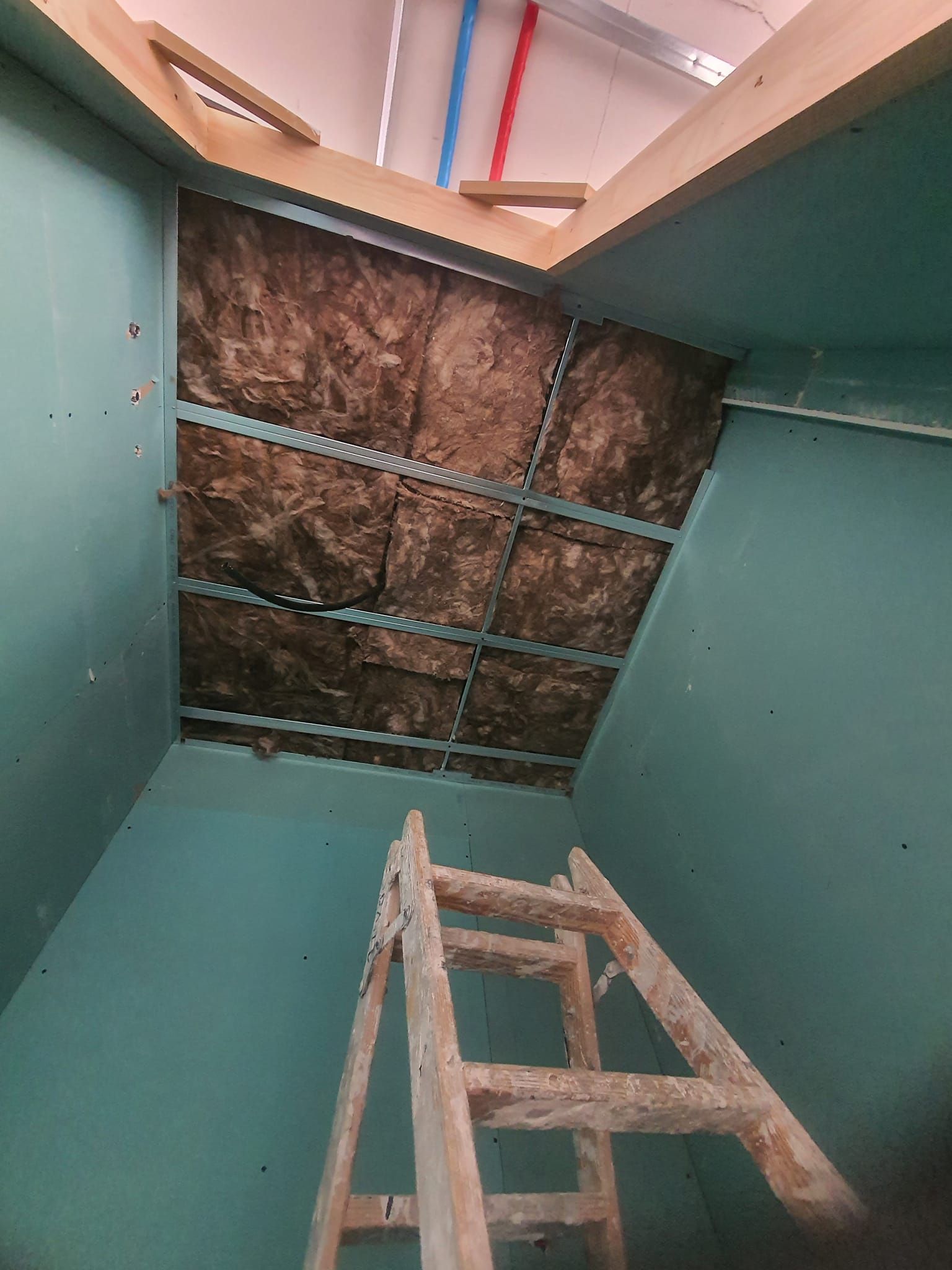 Interior con escalera, aislamiento y vigas de techo expuestas; paredes color verde azulado.