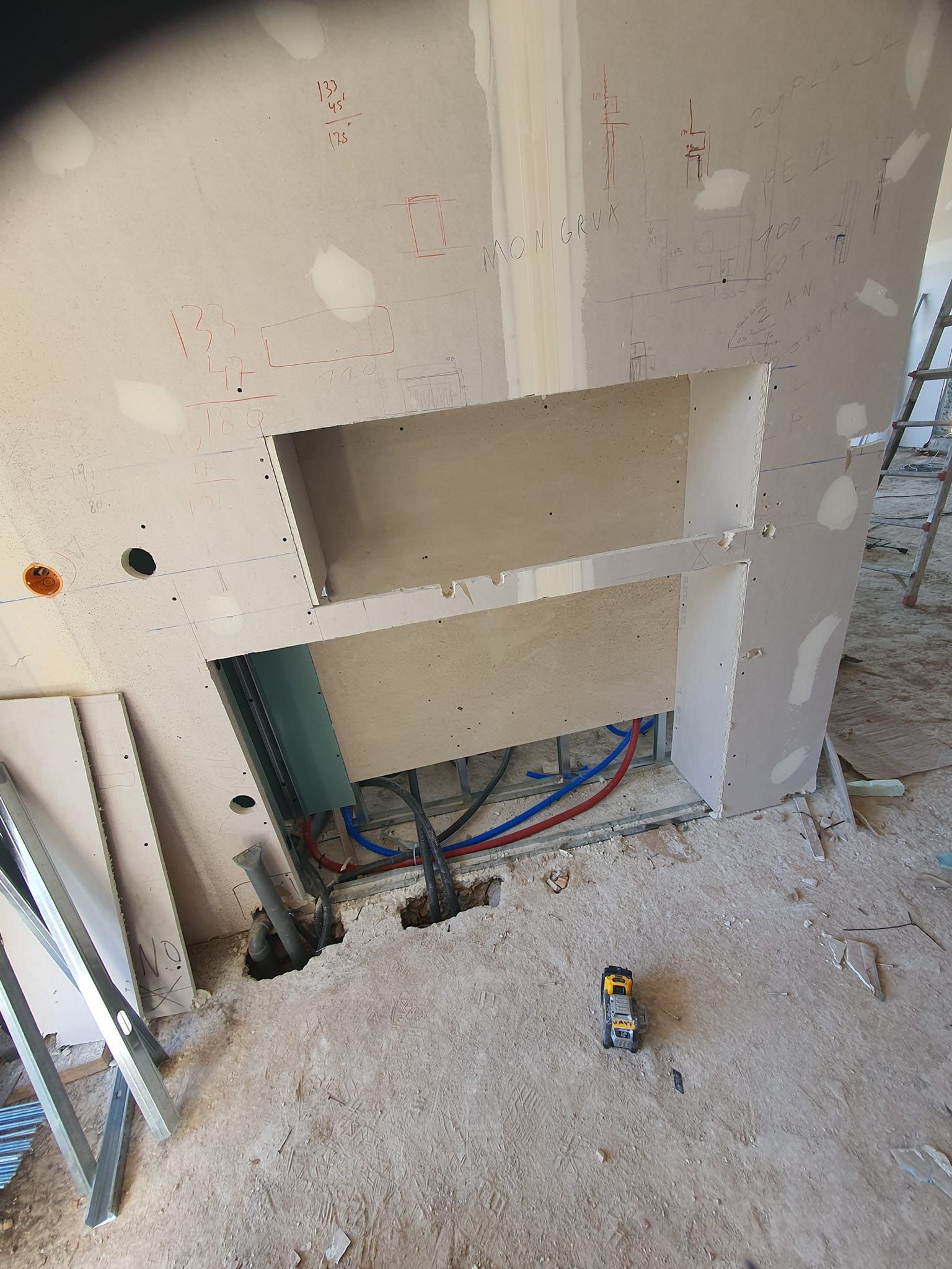 Construcción de paneles de yeso con estante incorporado y plomería visible en un sitio de construcción.