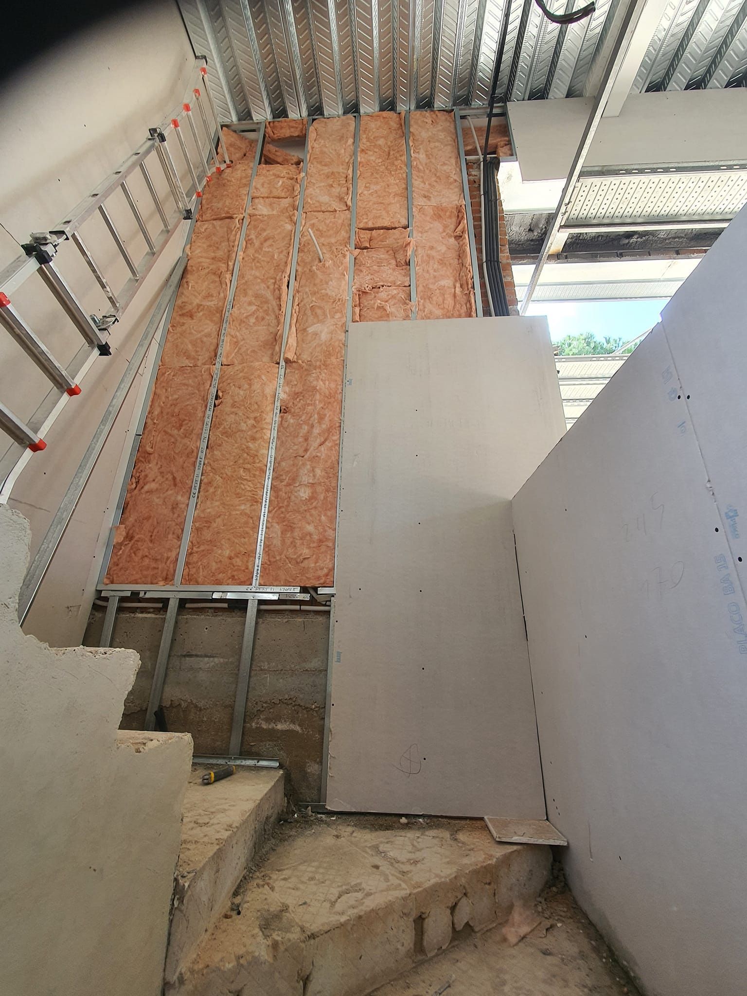 Construcción de escalera interior con drywall, aislamiento y estructura metálica.