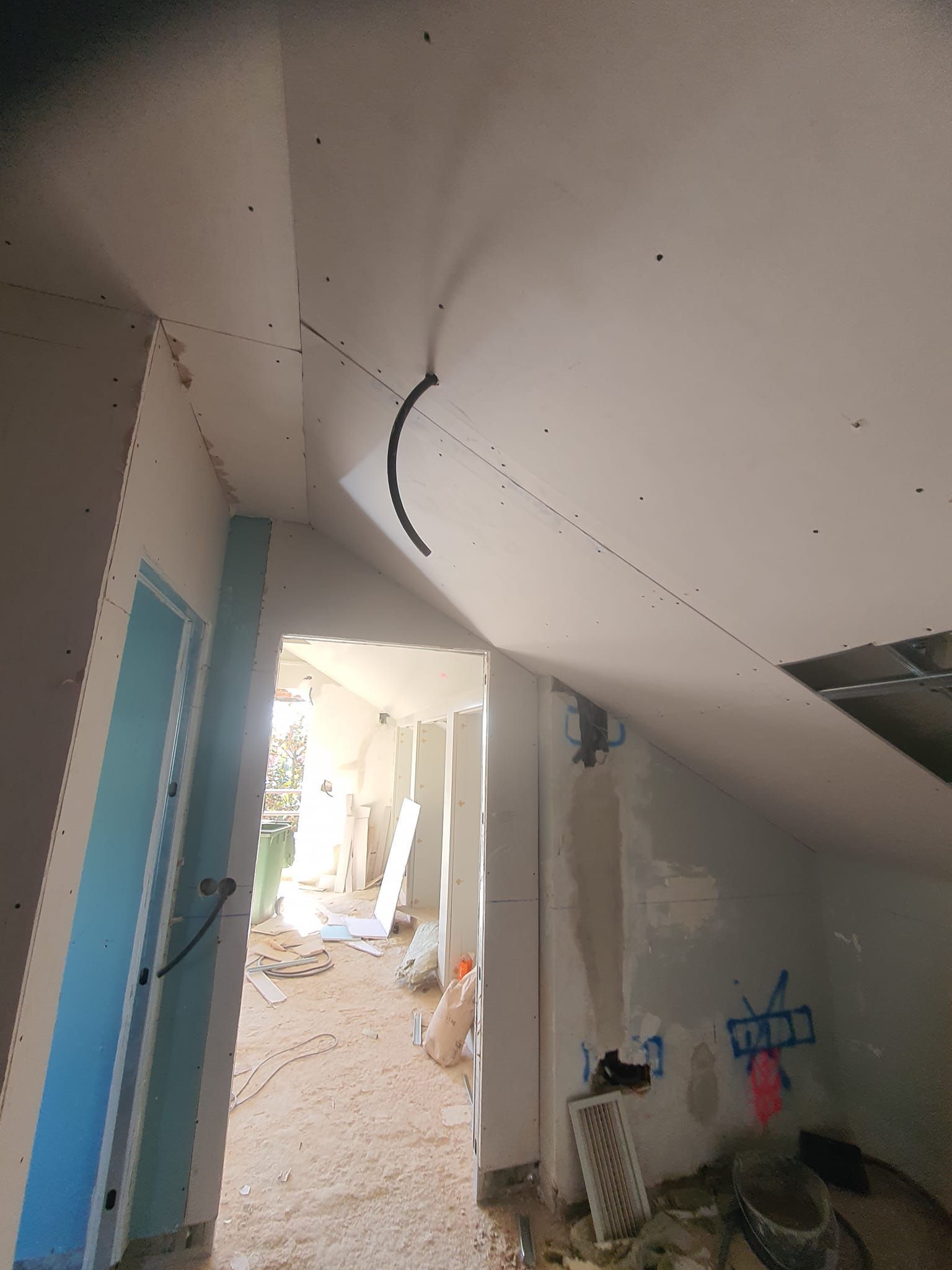 Obra: techo de yeso con sección arqueada; habitación con puerta azul, paredes sin terminar, escombros.