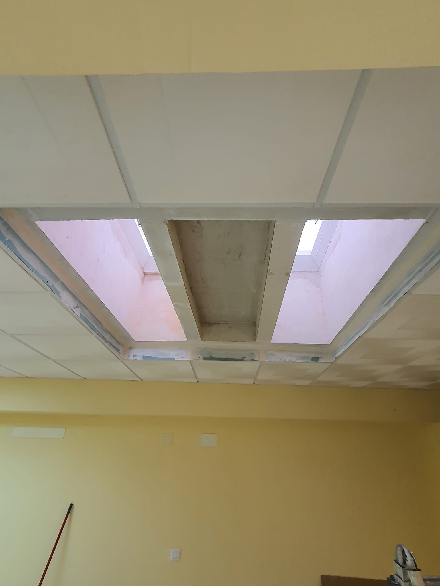 Techo con iluminación empotrada y paneles, sin terminar. Habitación con paredes amarillas.