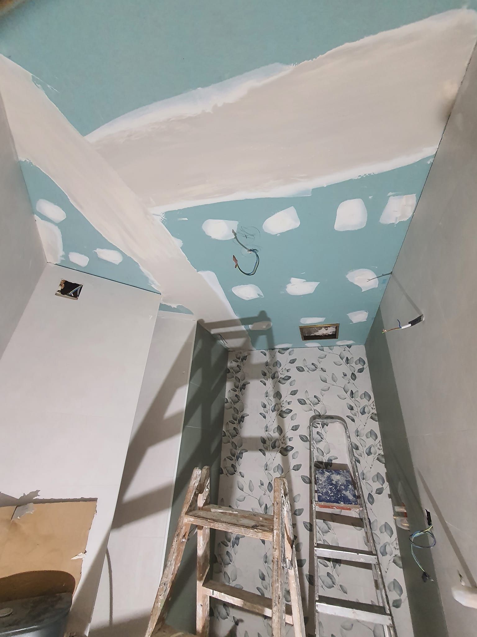 Construcción en una habitación; techo azul con paneles de yeso y vigas expuestas, dos escaleras están en el interior.