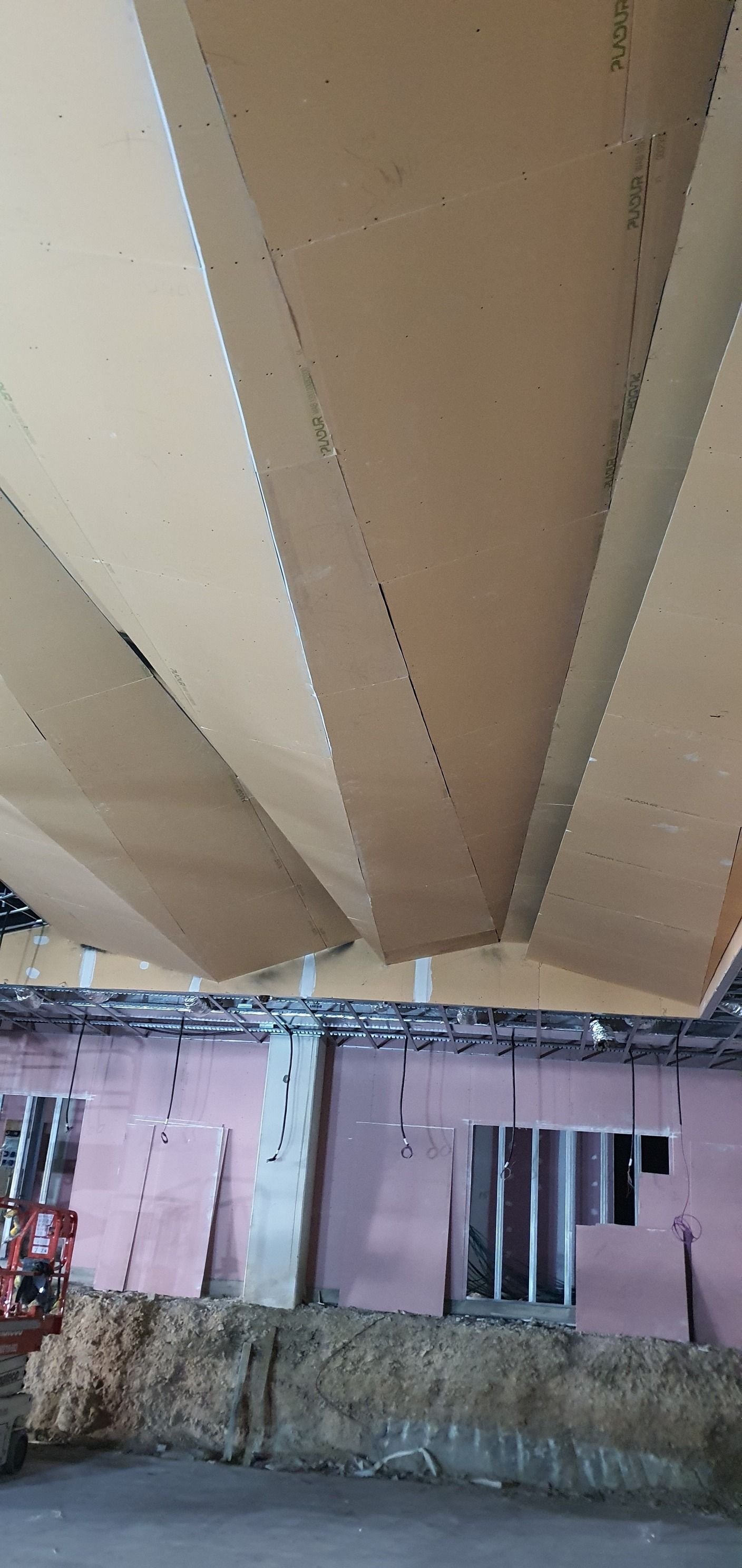 Interior de una obra en construcción con vigas de madera en ángulo en el techo y paredes aisladas de color rosa.