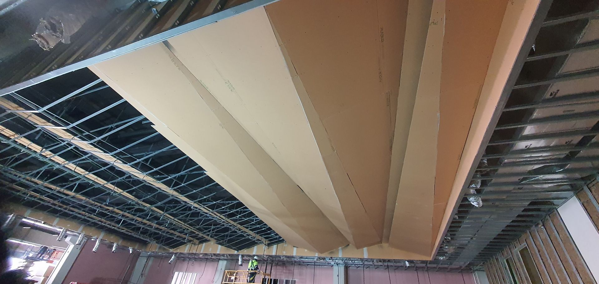 Construcción de un techo inclinado con estructura de metal expuesta y paneles de yeso sin terminar en un edificio.