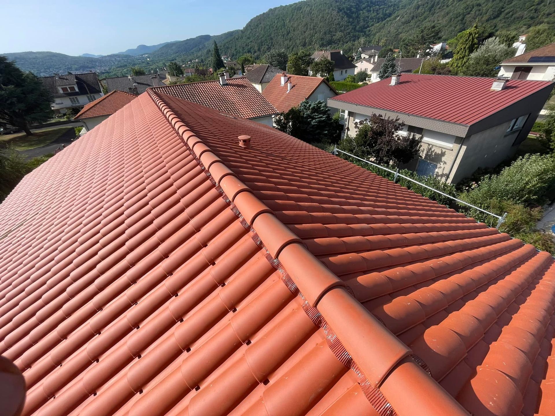Toit en tuiles de terre cuite rouge avec des montagnes en arrière-plan.