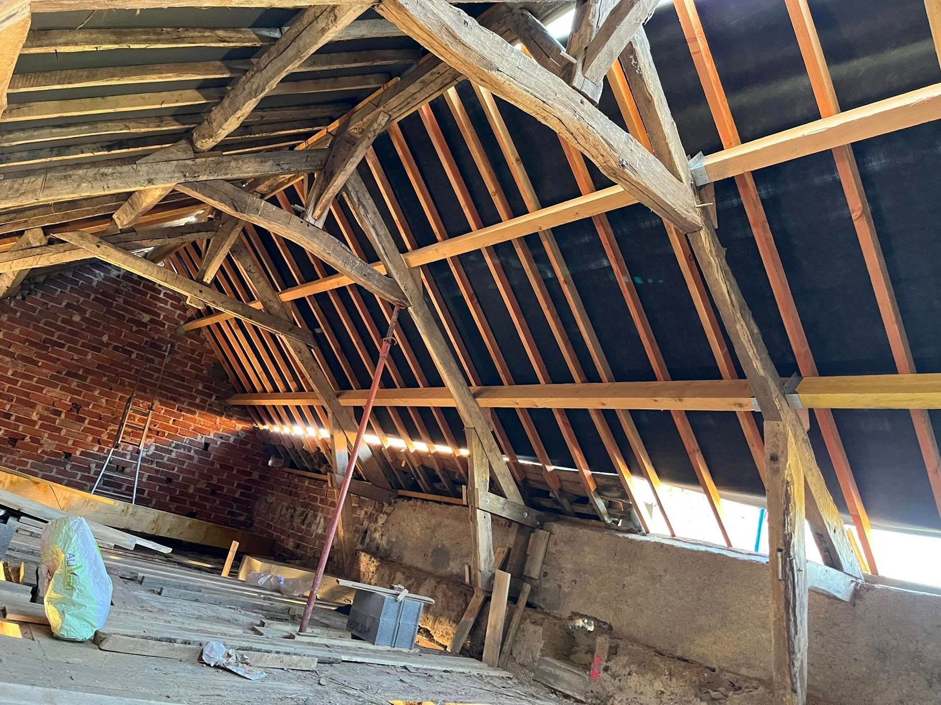 Vue intérieure d'un grenier en bois avec poutres apparentes et toiture sombre.