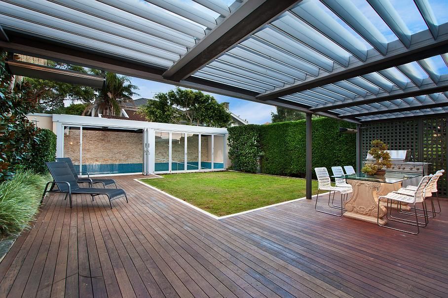 Terrasse couverte à l'arrière avec plancher en bois, sièges extérieurs et pelouse à côté d'une maison moderne