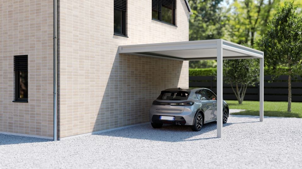 Voiture argentée garée sous un abri de voiture blanc moderne à côté d'une maison, avec un terrain gravillonné et des arbres à proximité.