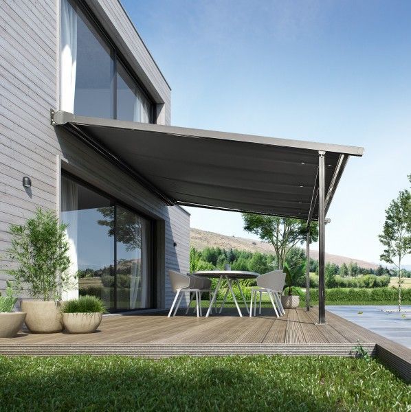Patio de maison moderne avec auvent gris, terrasse en bois, plantes en pot et table à manger extérieure installée dans un jardin ensoleillé