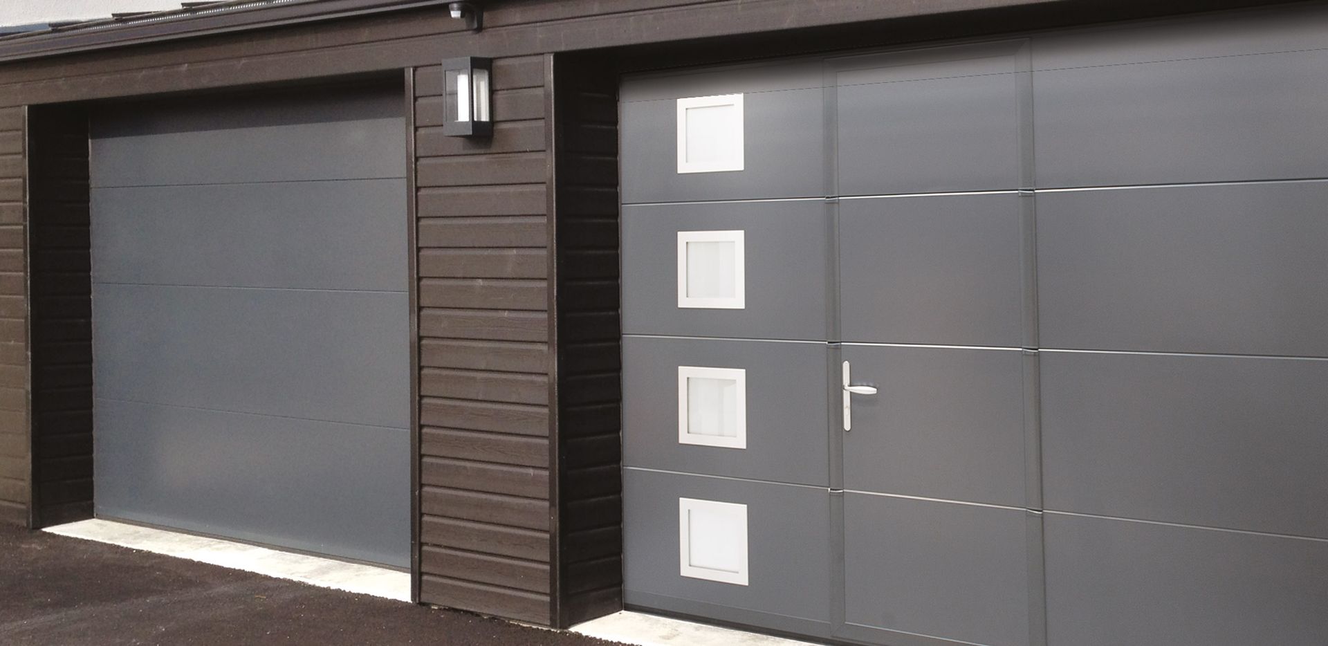 Garage moderne avec porte gris foncé assortie à la porte d'entrée et petites appliques murales