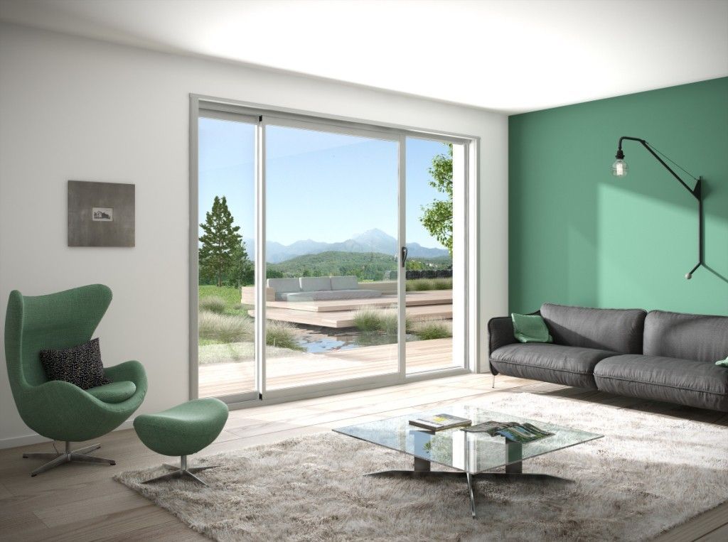 Salon moderne avec un mur d'accent vert, un canapé gris, un fauteuil et de grandes portes coulissantes en verre s'ouvrant sur un jardin.