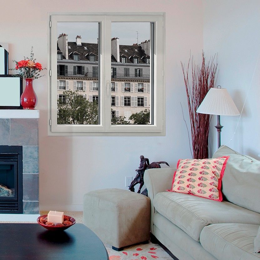 Salon confortable avec canapé beige, touches de rouge, cheminée et vue sur les bâtiments par la fenêtre