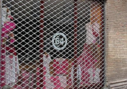 Magasin fermé avec une grille de sécurité métallique et des affiches rouges et blanches en vitrine.