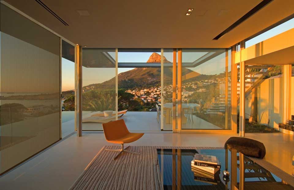 Patio moderne avec parois vitrées, chaise orange et vue sur le coucher de soleil sur les collines et l'eau.