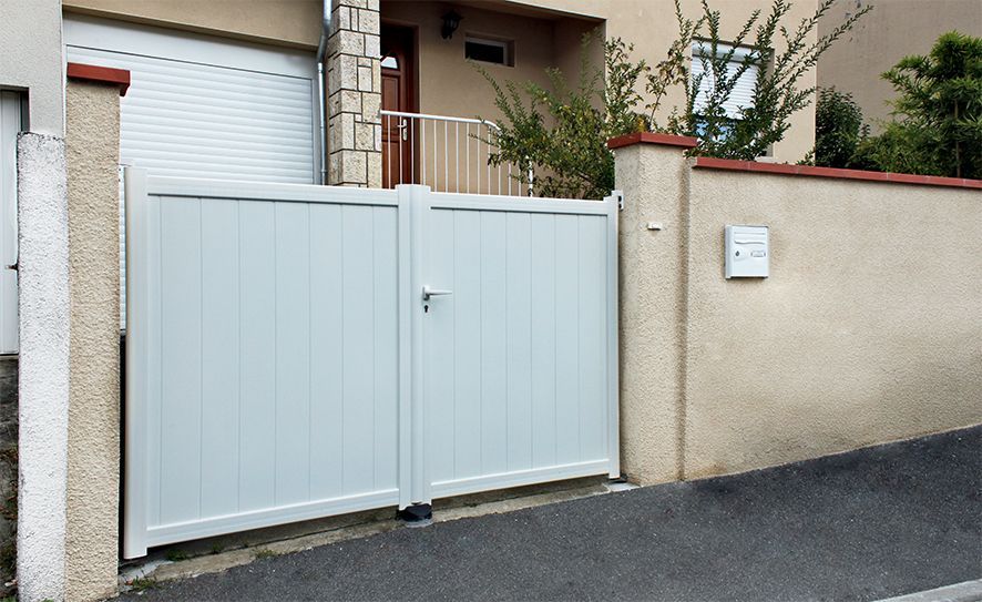 Portail d'allée en métal gris clair, adossé à un mur beige devant une maison.