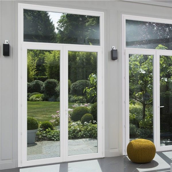 Des portes coulissantes en verre blanc s'ouvrent sur un jardin verdoyant, agrémenté de lanternes noires fixées au mur et d'un pouf jaune.