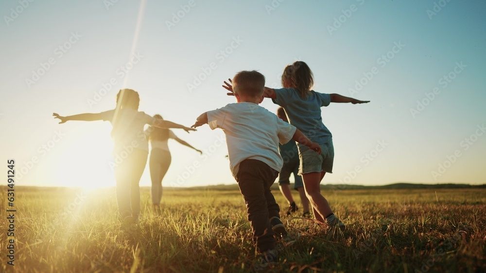 Bambini che corrono con le braccia tese in un campo illuminato dal sole al tramonto
