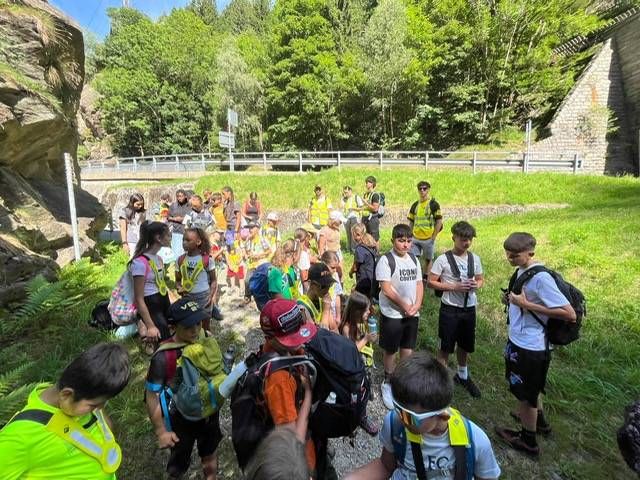 Bambini con zaini riuniti all'aperto su un sentiero erboso vicino a rovine di pietra e alberi.