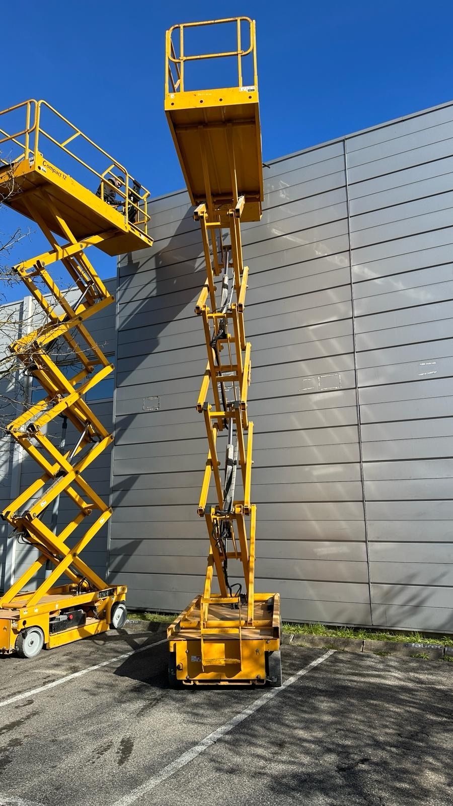 Deux nacelles jaunes déployées sur des places de parking