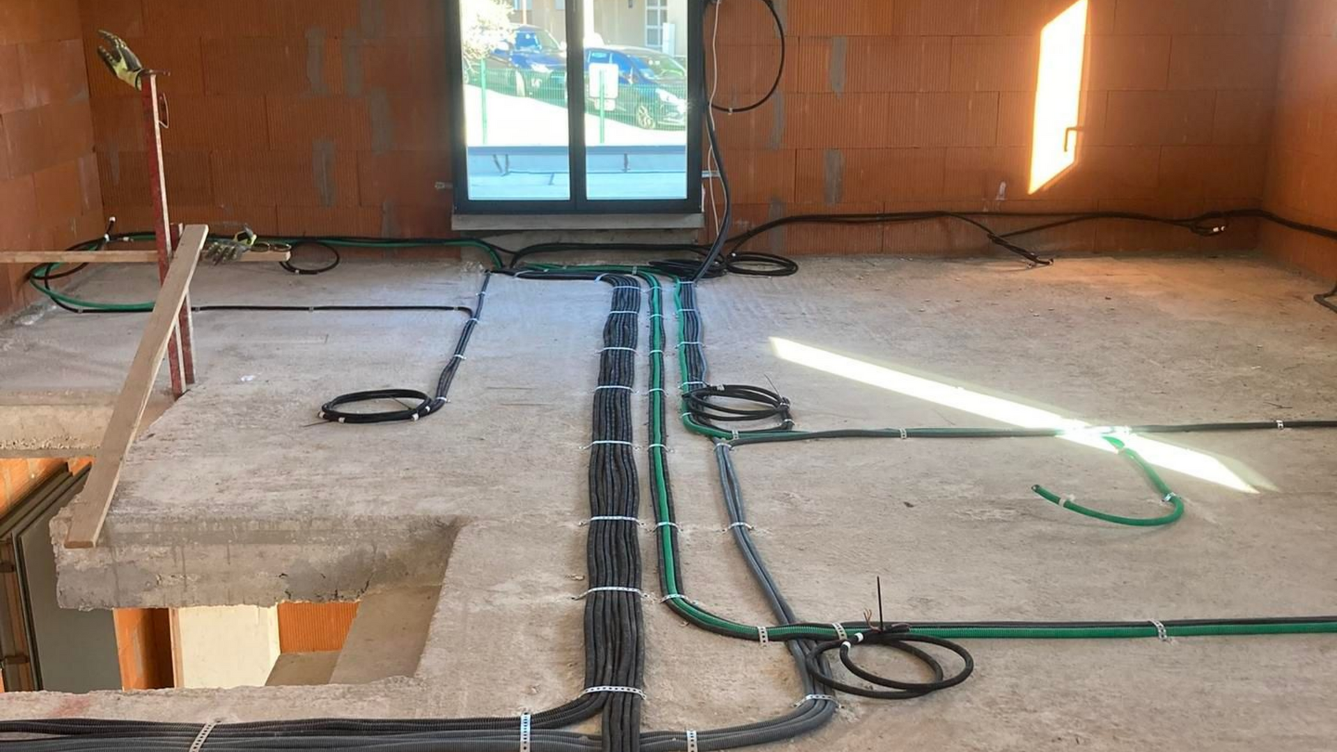 Câblage électrique sur un sol en béton pendant les travaux, avec câbles et conduits apparents.