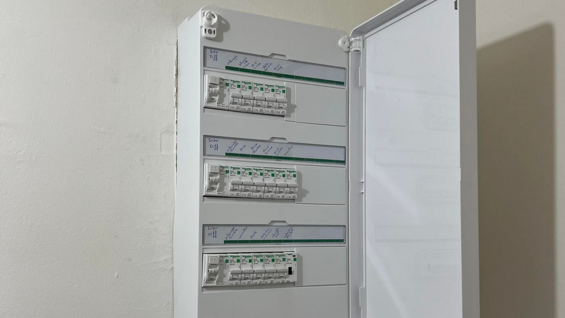 Tableau électrique blanc avec des rangées de disjoncteurs, fixé au mur.