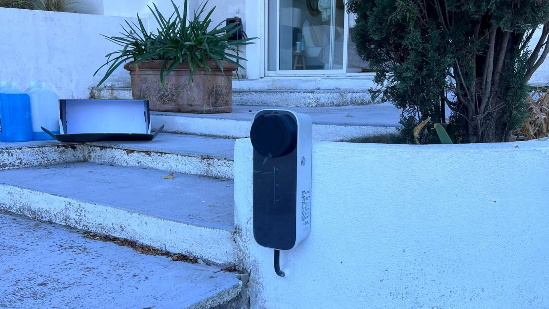 Borne de recharge pour véhicule électrique fixée sur un mur blanc à l'extérieur d'une maison.