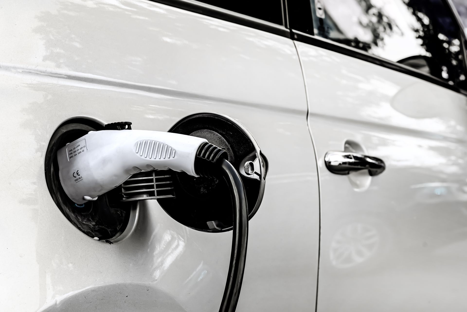 Voiture électrique blanche en charge, chargeur blanc branché sur le côté de la voiture.