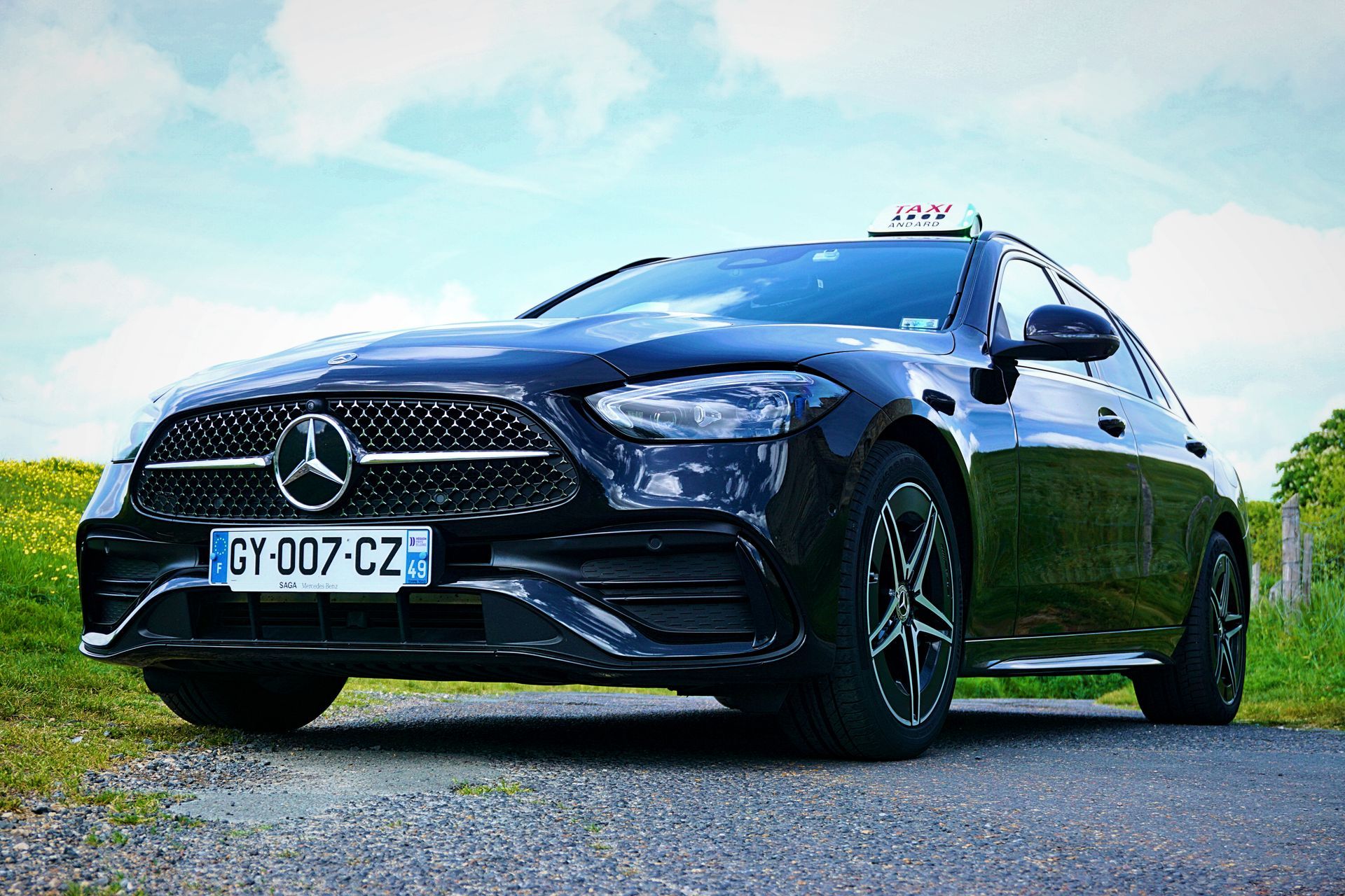 Une berline Mercedes-Benz noire garée en bord de route sous un ciel bleu