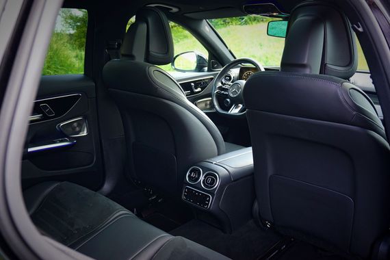 Vue de l'intérieur de la voiture depuis la banquette arrière, montrant les sièges en cuir noir et le tableau de bord avec les commandes de la console centrale.