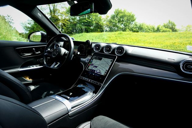 Intérieur de voiture avec tableau de bord et volant, vue sur l'herbe verte et les arbres à travers le pare-brise