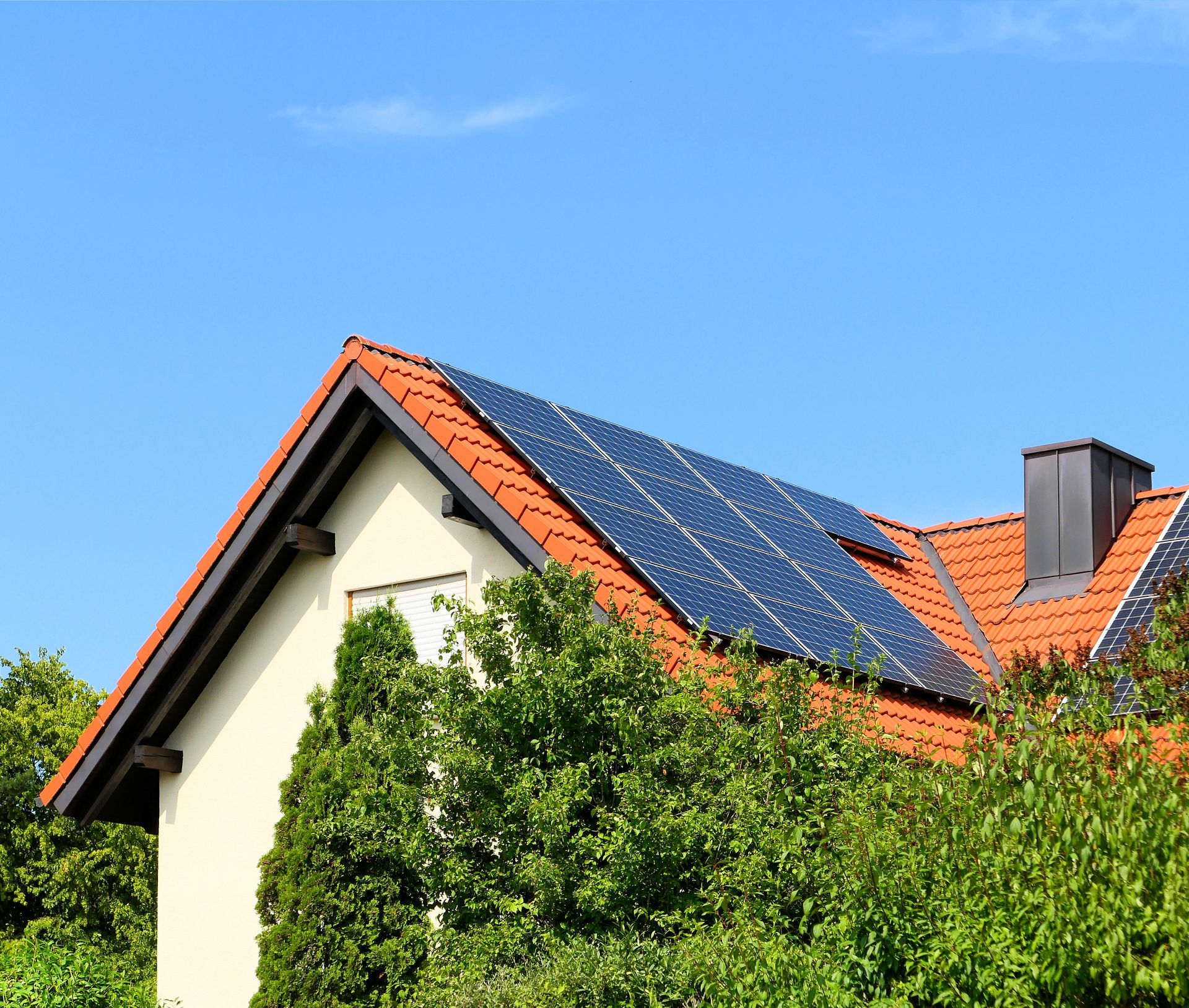 Une maison au toit de tuiles en terre cuite et dotée d'un grand ensemble de panneaux solaires sur le toit, partiellement dissimulés par des arbres verts.