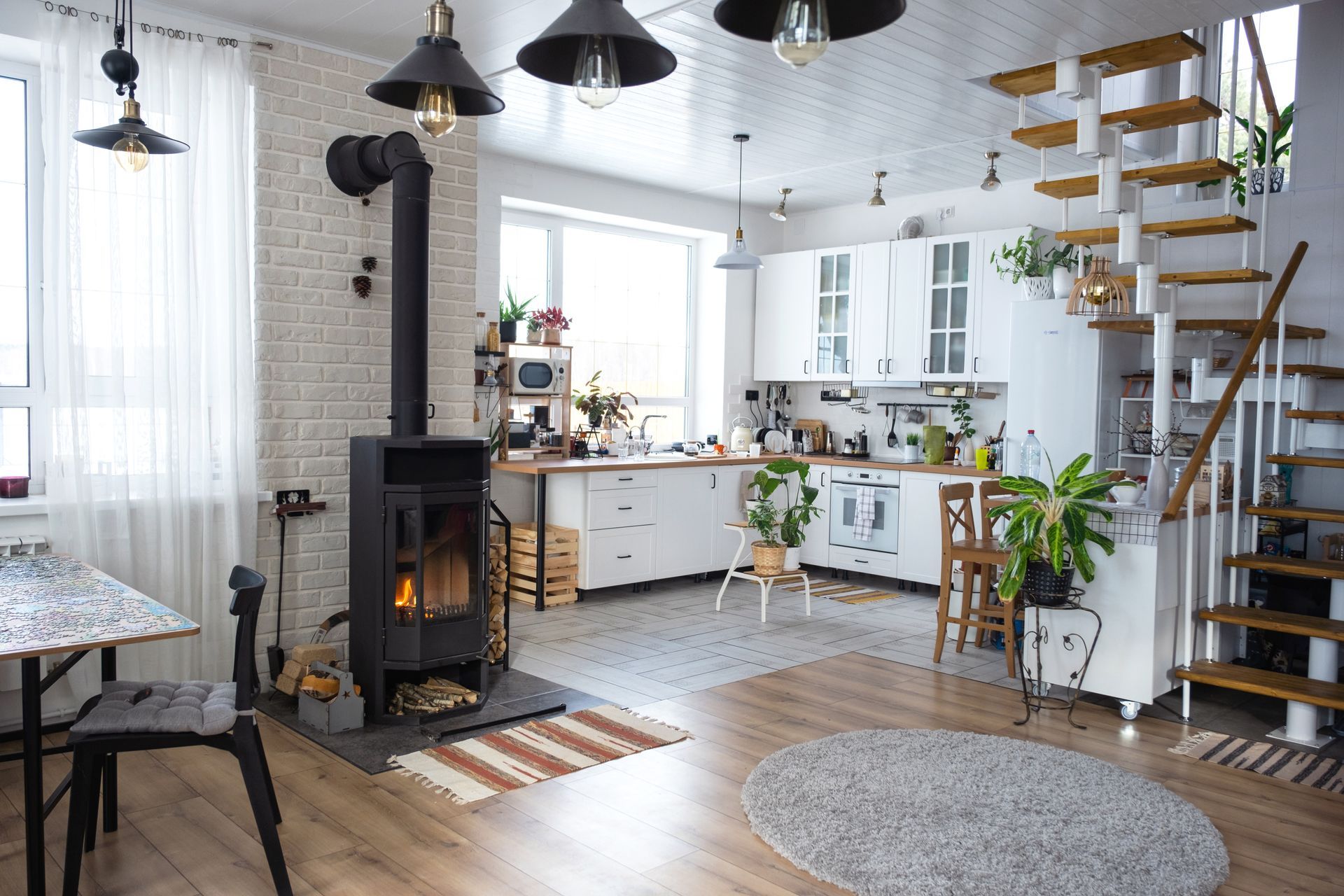 Une cuisine moderne avec des placards blancs, un poêle à bois et un escalier en bois, ouvert menant à une mezzanine.