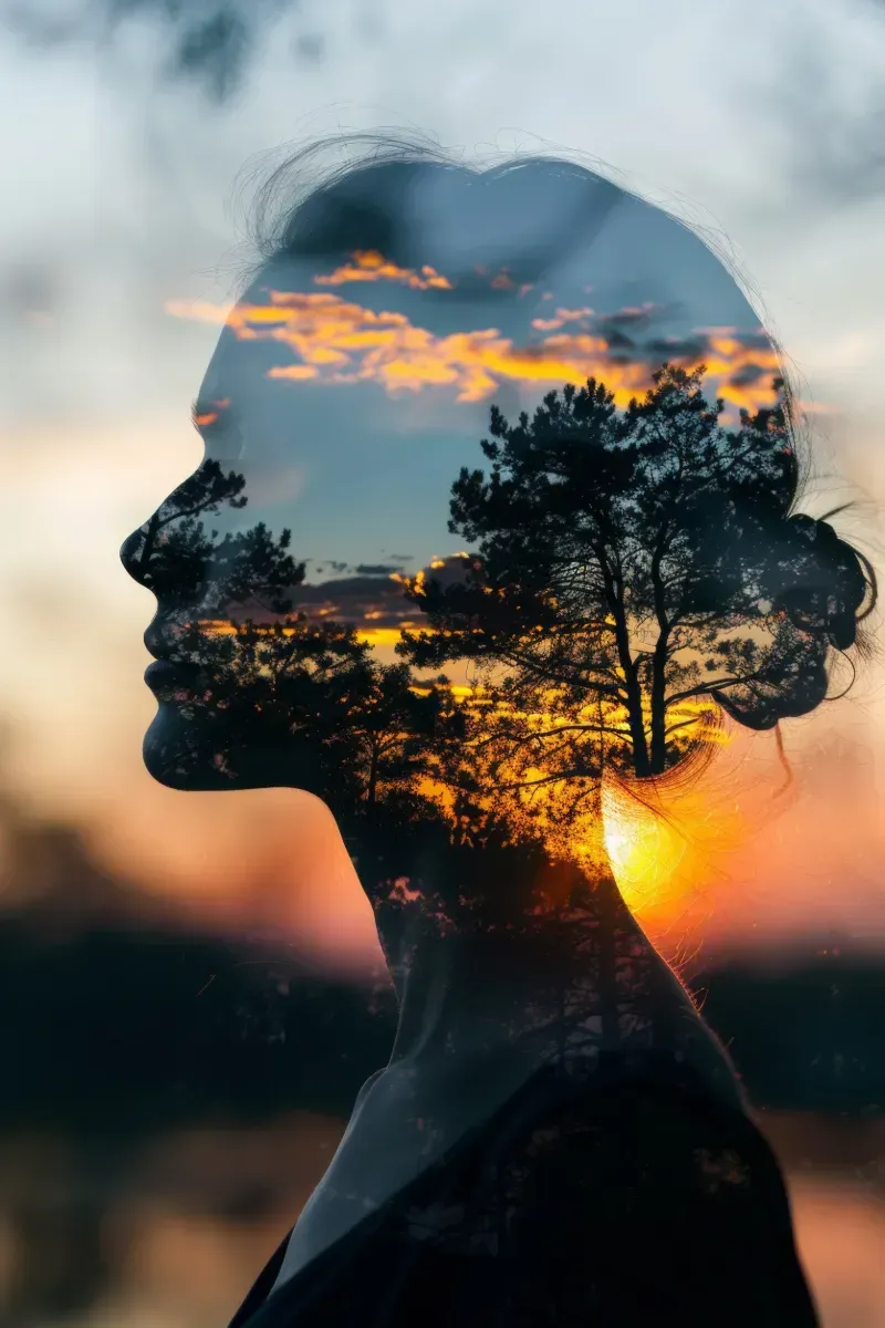 Una doble exposición del rostro de una mujer con una puesta de sol y árboles en su cabello.