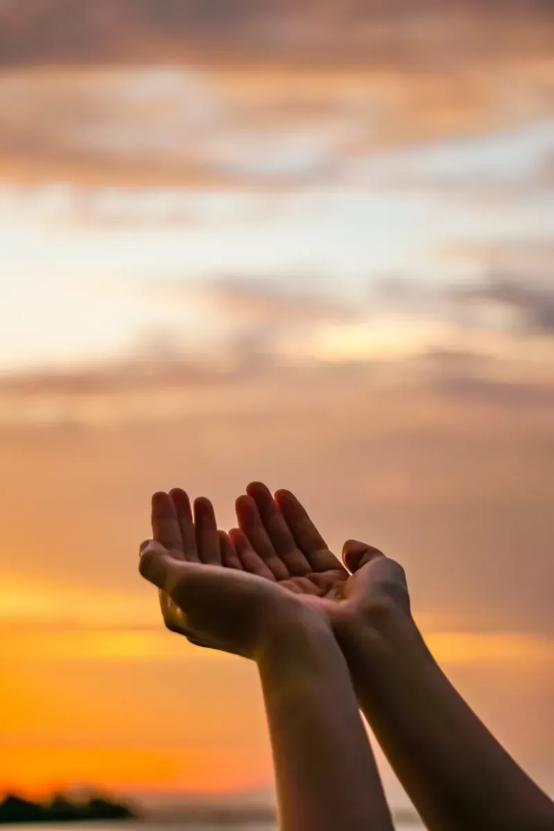 Una persona extiende sus manos frente a una puesta de sol.